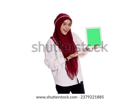 Beautiful excited Indonesian woman wearing hijab and head accessories holding a green scren tablet and looking at the camera 