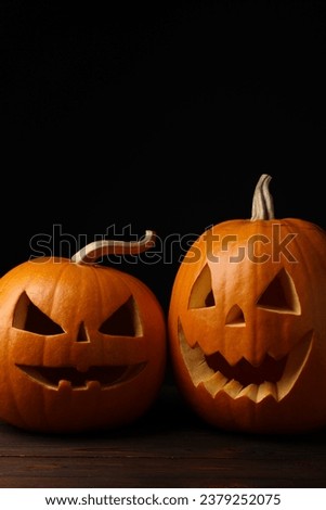 Scary jack o'lanterns made of pumpkins on wooden table in darkness, space for text. Halloween traditional decor