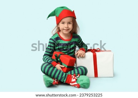 Cute little girl in elf costume with gift boxes on blue background