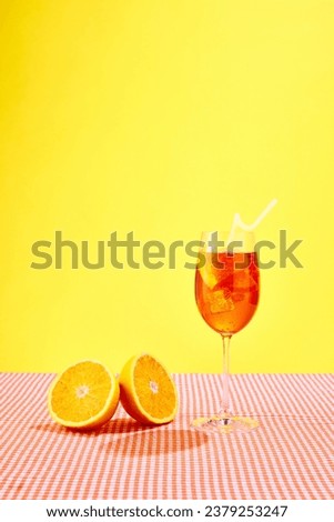 Glass of Aperol spritz cocktail with oranges standing on checkered tablecloth over yellow background. Summer vibe. Concept of alcohol drinks, party, holidays, bar, mix. Poster. Copy space for ad