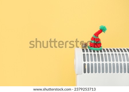 Electric convector heater with warm hat and coins near yellow wall at home. Heating saving concept