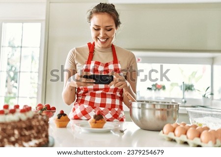 Young beautiful hispanic woman smiling confident make photo by smartphone to cupcake at the kitchen