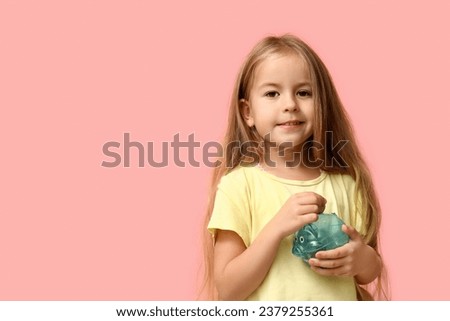 Cute little girl putting money into piggy bank on pink background