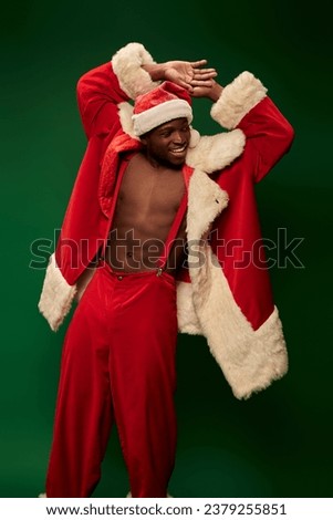 hot african american guy in christmas costume on shirtless body smiling and looking away on green