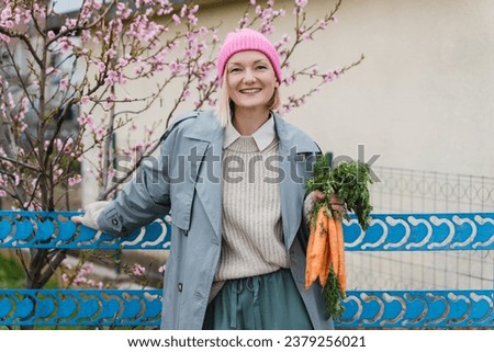 Young smiling woman with bouquet of fresh organic carrots in the garden outside. People doing conscious shopping of regional products from local market, sustainable food, no plastic packaging.