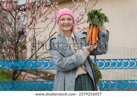 Young smiling woman with bouquet of fresh organic carrots in the garden outside. People doing conscious shopping of regional products from local market, sustainable food, no plastic packaging.