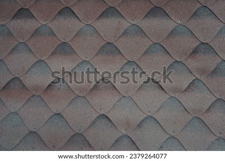 Fragment of the roof made of overlapping asphalt shingles. Texture and sinusoidal pattern of the old weathered asphalt shingles for background.  Royalty-Free Stock Photo #2379264077