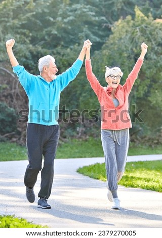 Smiling active senior couple jogging exercising and having fun and celebrating success rasing hands together taking a break in the park Royalty-Free Stock Photo #2379270005