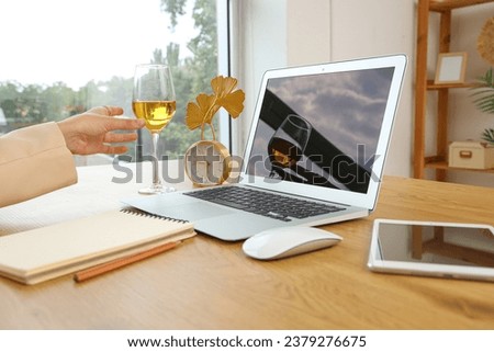 Woman with glass of wine and blank laptop at table in office, closeup
