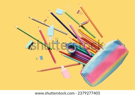 Flying pencil case and school stationery on yellow background Royalty-Free Stock Photo #2379277405