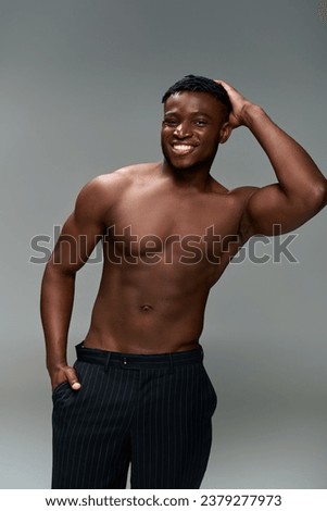 athletic african american man with shirtless body and hand in pocket smiling at camera on grey