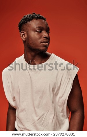 young african american fashion model in white tank top looking away on red and orange backdrop