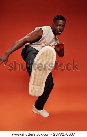 hot african american guy in striking pose with outstretched leg on red and orange backdrop