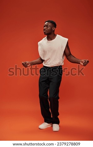 amazed and smiling african american man in trendy clothing looking away on red and orange backdrop