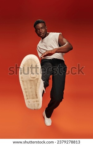 stylish african american man in daring pose with outstretched leg on red and orange backdrop
