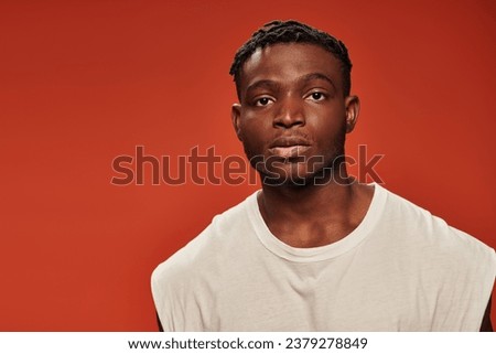 portrait of young handsome african american man in white tank top looking at camera on red backdrop