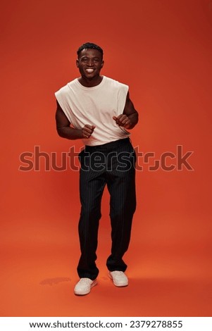 overjoyed african american man in fashionable casual clothes posing on red and orange backdrop