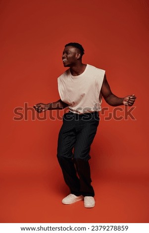 astonished and happy african american man in stylish outfit looking away on red and orange backdrop