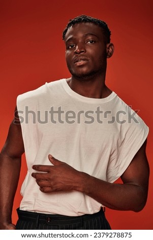 charismatic stylish african american man in white tank top looking at camera on red, modern style