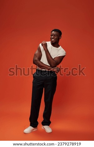 full length of joyful african american man in black pants standing on red and orange backdrop