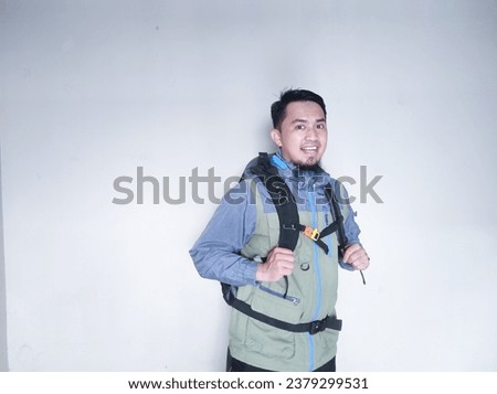 Asian adult man wearing a jacket and holding a bag with a happy expression while looking at the camera