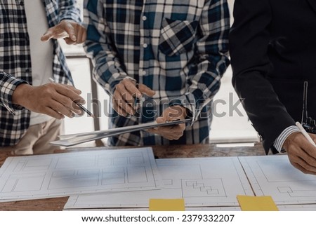 Three construction workers sit and discuss construction plans. A team of foremen and engineers talk with blueprints at the house construction site to check the house plans before starting work.
