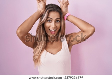 Young blonde woman standing over pink background posing funny and crazy with fingers on head as bunny ears, smiling cheerful 