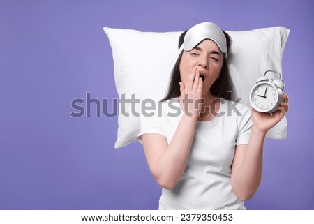 Tired young woman with sleep mask, alarm clock and pillow on purple background, space for text. Insomnia problem Royalty-Free Stock Photo #2379350453