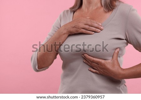 Woman doing breast self-examination on pink background, closeup