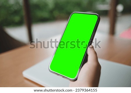 Mockup image of a business people holding smart mobile phone with blank green screen on vintage wooden table in modern cafe restaurant during meeting or lunch.	
