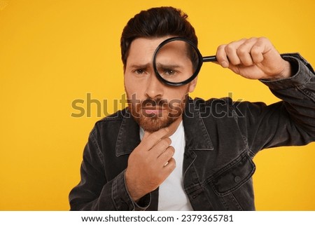 Man looking through magnifier glass on yellow background Royalty-Free Stock Photo #2379365781