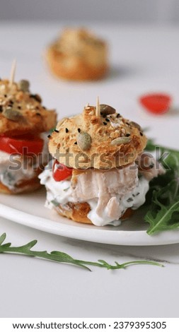 Homemade wholesome burgers featuring whole grain buns studded with sesame and pumpkin seeds, paired with chicken fillet, fresh tomatoes, arugula, and a tangy yogurt sauce