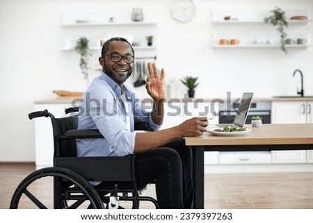 Salad placed on writing desk near laptop by african person with disability in dining room. Happy business manager enjoying healthy food while telecommuting in home office at midday showing sign ok