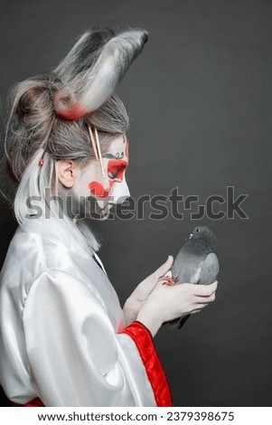 Beautiful young woman in Halloween makeup and costume holding bird on black background
