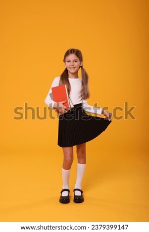Happy schoolgirl with books on orange background Royalty-Free Stock Photo #2379399147