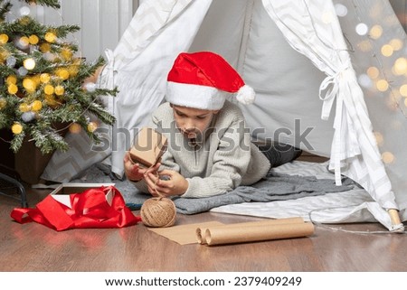 Family Christmas. Children open Christmas presents. A teenage boy in a Santa hat opens a gift and smiles while sitting on the floor of the house