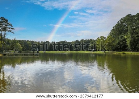 a beautiful summer landscape at Huddleston Pond Park with a lake surrounded by lush green trees, grass and plants, blue sky, clouds and a rainbow in Peachtree City Georgia USA