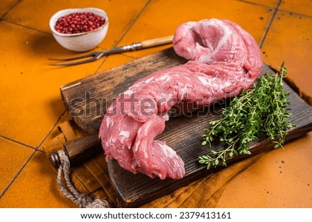 Fresh Raw pork tenderloin fillet meat on a wooden board with thyme. Orange background. Top view.