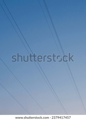 Diagonal geometry composition of taut power lines against a clear blue-pink gradient sky with a grainy effect