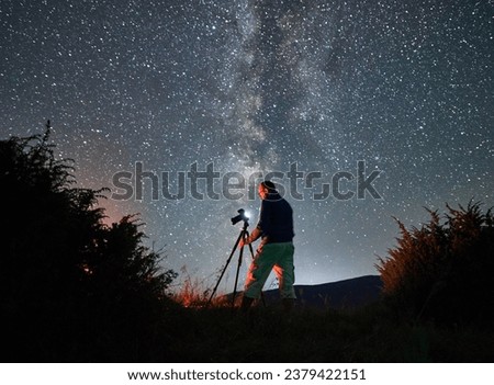 Professional photo shoot of Milky Way in mountains. Male photographer taking photos of starry night in mountains. Back view of man with camera.