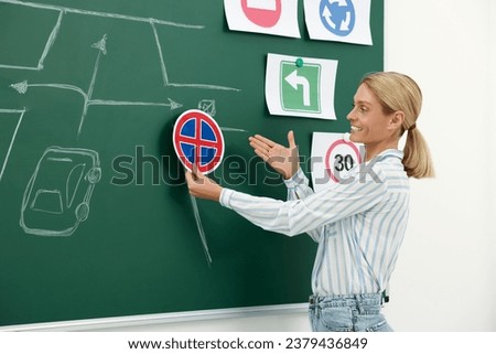 Teacher showing No Stopping road sign near chalkboard during lesson in driving school