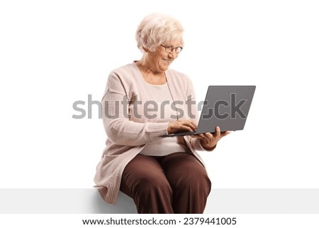 Elderly woman sitting on a blank panel and using a laptop computer isolated on white background