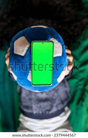 Woman holding smartphone with green screen on blue soccer ball