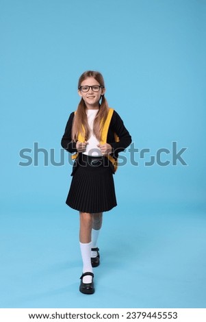 Happy schoolgirl with backpack on light blue background Royalty-Free Stock Photo #2379445553