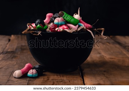 Halloween candies in big black bowl sweet fingers, brains and spiders on wooden background with copy space