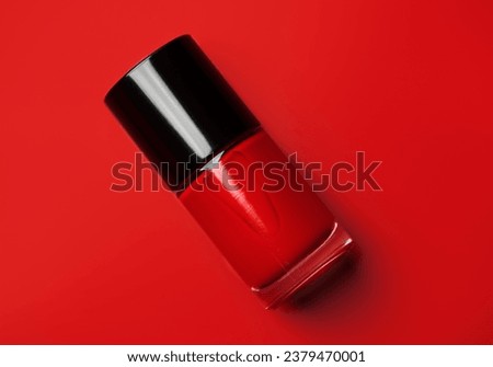 Red nail polish bottle over bright red background, top view. Gel nailpolish,  shellac UV, bottle with brush, varnish, manicure concept, Beauty salon. Glass bottle close up. Nail care product. 