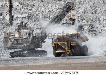 ELECTRIC ROPE SHOVEL LOADING AN ELECTRIC MINING TRUCK ON AN OPEN PIT MINE Royalty-Free Stock Photo #2379473375