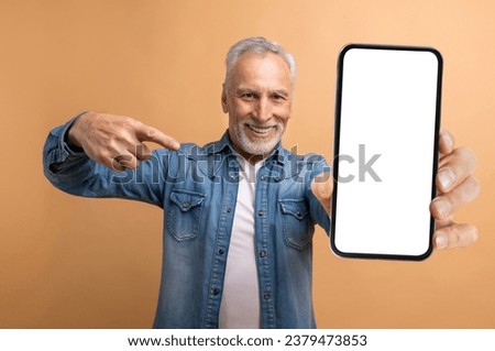 Nice online offer. Handsome cheerful stylish grey-haired mature man wearing casual outfit holding huge cell phone with white blank screen, using smartphone, isolated on beige background, mockup