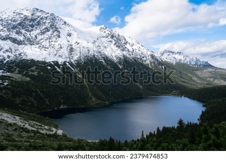 Morskie Oko Snowy Mountain Hut in Polish Tatry mountains, drone view, Zakopane, Poland. Aerial view shot of beautiful green hills and mountains in dark clouds and reflection on the lake Morskie Oko