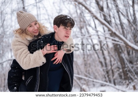 A young couple walks in the park in winter. Guy and girl hugging outdoors.